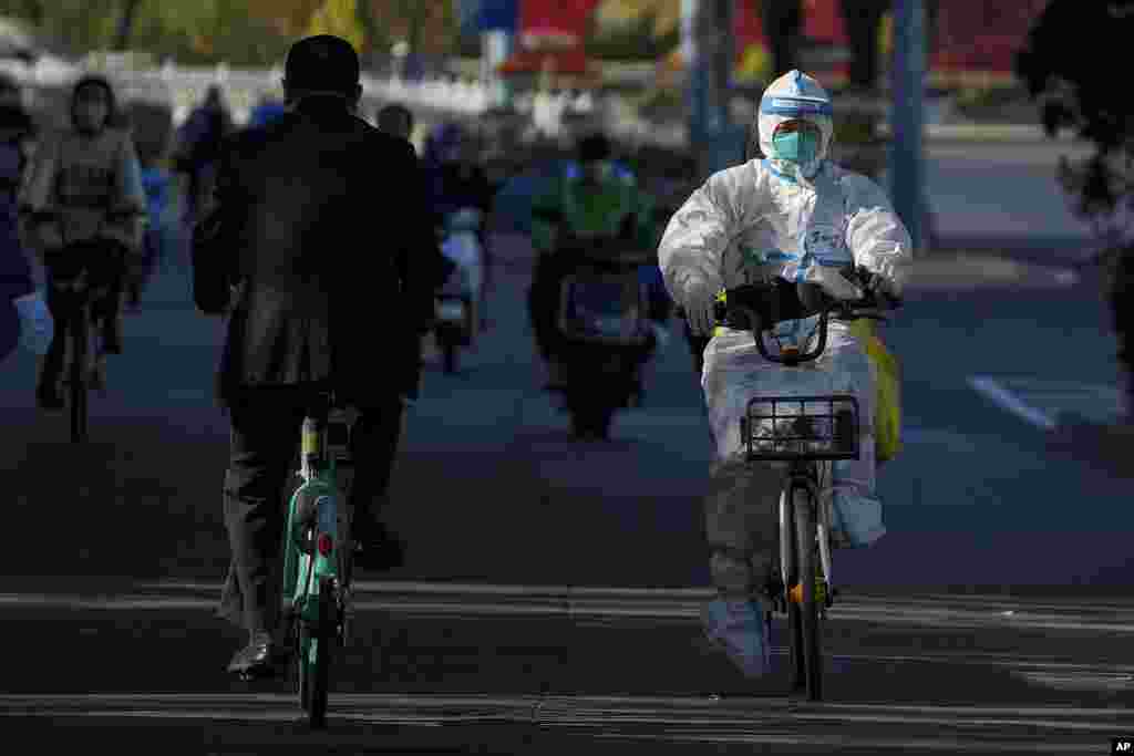 A worker in protective gear rides on a street as she heads to take COVID-19 samples from residents who have been under home quarantine in Beijing. The ruling Communist Party is enforcing a "Zero COVID" policy that has closed areas throughout China for weeks to try to isolate every case.&nbsp;