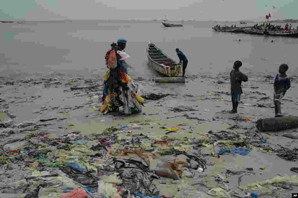 Kids look at environmental activist Modou Fall, who many simply call "Plastic Man", while he walks on the Yarakh Beach littered by trash and plastics in Dakar, Senegal.