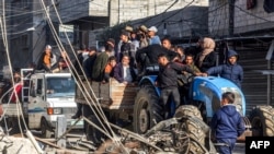 Orang-orang mengendarai gerobak yang ditarik traktor melewati puing-puing bangunan yang hancur dan menara masjid di Rafah, Jalur Gaza selatan, 14 Februari 2024. (MOHAMMED ABED / AFP)
