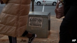 Women pass a sticker advertising abortion pills on a sidewalk in Johannesburg, June 28, 2023.