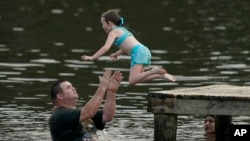 John Crouch membantu seorang anak perempuan berenang untuk mendinginkan tubuh dari cuaca panas di Ross Barnett Reservoir di Bobby Cleveland Park, Lakeshore di Rankin County, Mississippi, Jumat, 30 Juni 2023. (Foto: Rogelio V. Solis/AP)