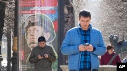 Men look at their phones walking past an army recruiting billboard with the words 'Military service under contract in the armed forces,' in St. Petersburg, Russia, Apr. 12, 2023. 