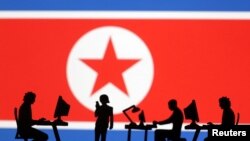 ภาพเงาคนทำงานงานกับคอมพิวเตอร์ ที่ด้านหน้าธงเกาหลีเหนือ (Reuters)