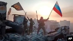 FILE - In this grab taken from video released by Prigozhin Press Service on May 20, 2023, Yevgeny Prigozhin's Wagner Group military company members wave a Russian national and Wagner flag atop a damaged building in Bakhmut, Ukraine.