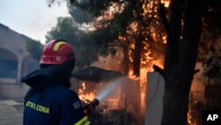 A firefighter works to extinguish the flames at a burning house in northern Athens, Aug. 12, 2024, as hundreds of firefighters tackle a major wildfire. Dry pine forests and strong winds have aided the fire, making it difficult for firefighters to get the blaze under control.  