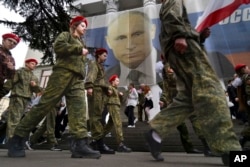 FILE - Youths help mark the ninth anniversary of the Crimea annexation from Ukraine with the banner reading "Russia doesn't start wars, it ends them," next to an image of Russian President Vladimir Putin in Yalta, Crimea, March 17, 2023.