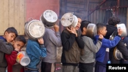 Anak-anak Palestina membawa panci antre untuk mendapat makanan dari sebuah dapur amal di tengah kekurangan pasokan pangan akibat konflik Israel dan Hamas yang masih berlangsung, di Rafah, Jalur Gaza, 14 Desember 2023. (Foto: Saleh Salem/Reuters)
