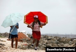 Siswa memegang payung saat berjalan pulang dekat Terminal Kontainer Internasional Jakarta, 13 Januari 2010. (Foto: REUTERS/Beawiharta)