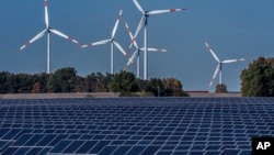 Turbin angin berputar di belakang pembangkit listrik tenaga surya di kota Rapshagen, Jerman (foto: ilustrasi). Uni Eropa selidiki dua produsen panel surya yang diduga mendapat subsidi pemerintah China. 