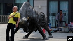 资料照：一名男子靠在北京一家证券交易所前的公牛铜像上。（2021年5月19日）