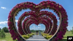 A woman swings from a heart-shaped flower installation in Dobro Park, Motyzhyn, Kyiv region, Ukraine, June 26, 2024. Despite hardships brought by war flowers fill Kyiv and other Ukrainian cities. 