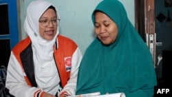 Lingga Permesti, left, a legislative candidate for Indonesia's Islamic Prosperous Justice Party (PKS), presents a calendar to a resident during house visitations ahead of the election in Klaten, Central Java, Jan. 18, 2024.