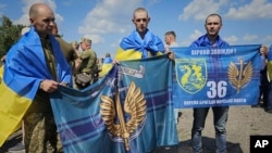 In this photo provided by the Ukrainian Presidential Press Office on July 17, 2024, Ukrainian prisoners of war hold Marine flags as they pose for a photo after a prisoners exchange at an undisclosed location in Ukraine.