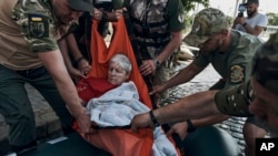 Emergency workers evacuate an elderly resident on a rubber boat from a flooded neighborhood in Kherson, Ukraine, June 7, 2023. 