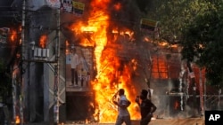 FILE - Men run past a shopping center which was set on fire by protesters during a rally against Prime Minister Sheikh Hasina and her government, in Dhaka, Aug. 4, 2024. 