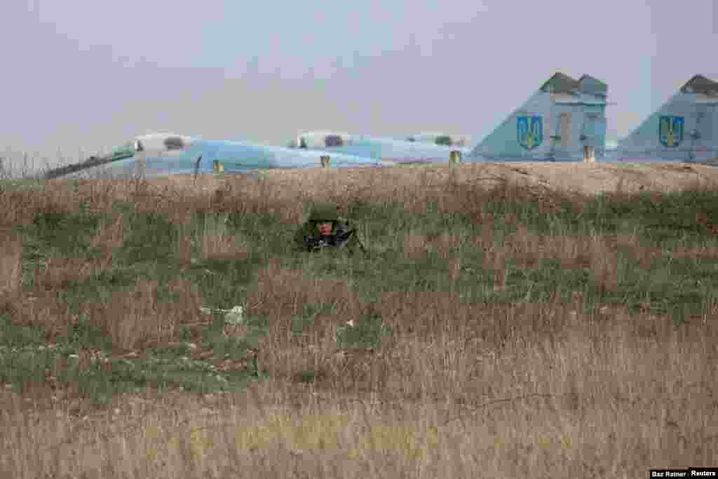 Un soldado ruso observa al personal militar ucraniano en el aeropuerto de Belbek, cerca de Sebastopol. La base de la Fuerza Aérea de Ucrania se convirtió en una de las últimas posiciones ucranianas en Crimea ya que su comandante se negó a entregar el sitio a las tropas rusas. Finalmente fue detenido por las fuerzas rusas y el personal ucraniano fue expulsado.