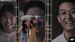 FILE - Women carrying umbrellas walk by frames displaying portraits of workers in a Chinese liquor industry on display at a shopping street in Beijing, July 25, 2023.