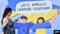 FILE - A woman walks past a placard reading "Let's rebuild Ukraine together!" in the center of Ukrainian capital of Kyiv, May 24, 2023.