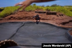 Kekanemekala Taniguchi smooths wet black clay onto the wall of a salt bed in the Hanapepe salt patch on July 12, 2023, in Hanapepe, Hawaii. AP Photo/Jessie Wardarski)