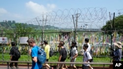 Visitors pass by a wire fence decorated with ribbons written with messages wishing for the reunification of the two Koreas at the Imjingak Pavilion in Paju, South Korea, near the border with North Korea, Wednesday, July 19, 2023.(AP Photo/Ahn Young-joon)