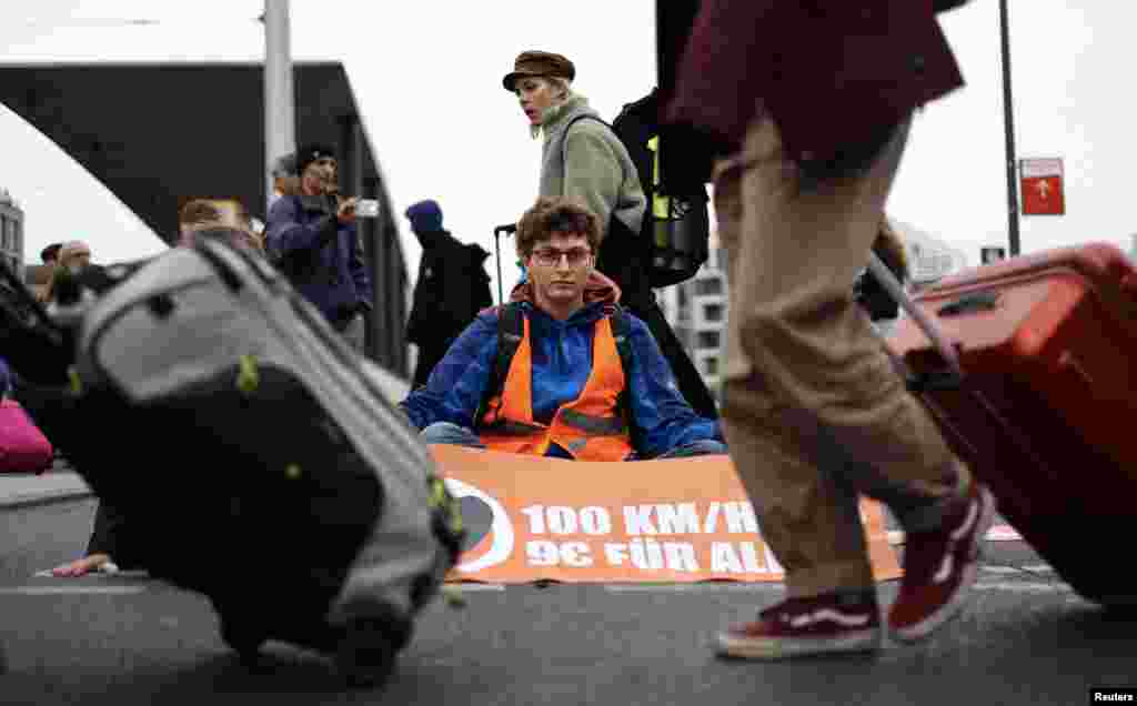 Passengers pull their trolleys past an environment activist of "Last Generation" who glued himself with super glue to a street outside the main railways station during climate change protests in Berlin, Germany.