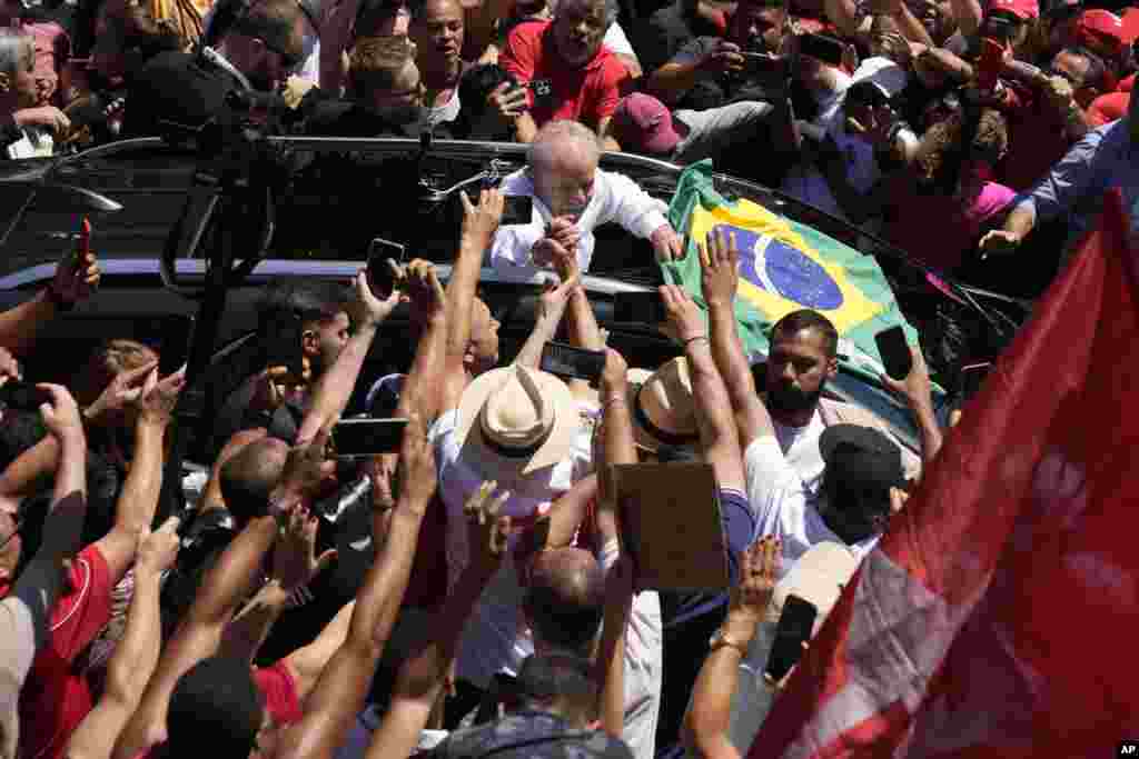 Former Brazilian President Luiz Inacio Lula da Silva, center, who is running for president again, hold hands with a supporter after voting in a presidential run-off election in Sao Paulo, Brazil.