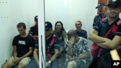 Sejumlah petugas polisi menjaga Mikhail Zorin (kiri, duduk), Svetlana Timofeeva (tengah, belakang), dan Fedir Alpatov (duduk, kanan) dalam persidangan di pengadilan Elbasan, Albania, pada 24 Agustus 2022. (Foto: AP/Franc Zhurda)