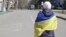 FILE - A woman covered by Ukrainian flag stands in front of Russian troops in a street during a rally against Russian occupation in Kherson, Ukraine, March 19, 2022. 