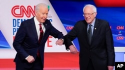 Bivši potpredsednik SAD Džozef Bajden i senator iz Vermonta Berni Sanders pozdravljaju se laktovima pred početak debate u studiju kablovske mreže CNN u Vašingtonu u nedelju 15. marta 2020. (Foto: AP/Evan Vucci)