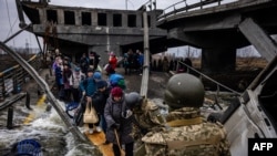 Evacuees cross a destroyed bridge as they flee the city of Irpin, northwest of Kyiv, Ukraine, March 7, 2022.