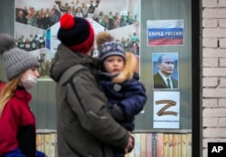 FILE - A family walk past a portrait of Russian President Vladimir Putin, a sign reading 'Go Russia!' and the letter Z, which has become a symbol of the Russian military, displayed in the window of a children's library in St. Petersburg, March 11, 2022.