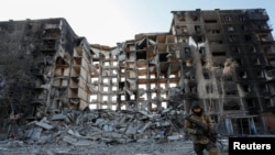 A service member of pro-Russian troops walks near an apartment building destroyed in the course of Ukraine-Russia conflict in the besieged southern port city of Mariupol, Ukraine, March 28, 2022.