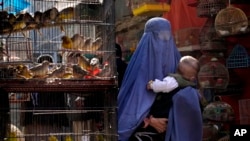 FILE - A woman wearing a burqa walks through a bird market as she holds her child, in downtown Kabul, Afghanistan, May 8, 2022. 