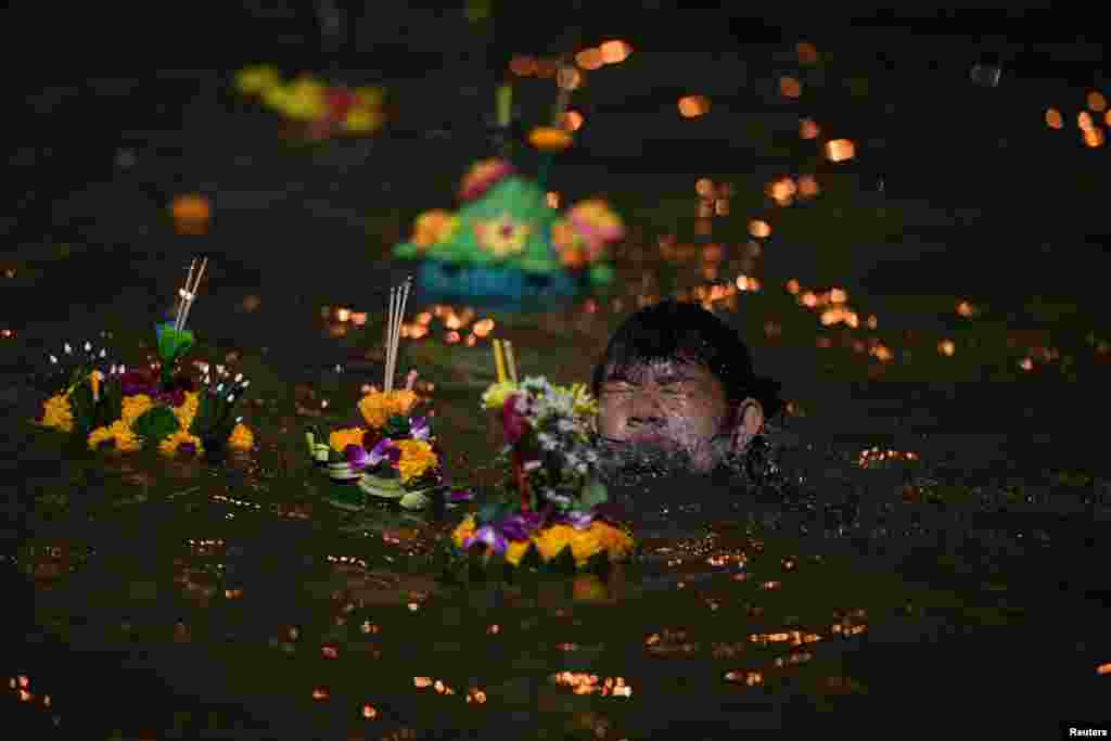 A boy swims in Chao Phraya River as he helps to place a Krathong, or a "floating basket", in the water during the Loy Kratong festival in Bangkok, Thailand.