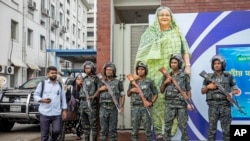 FILE - Military personnel stand guard in front of a large cutout portrait of Prime Minister Sheikh Hasina in Dhaka, Bangladesh, July 30, 2024. Interim leader Muhammad Yunus said, Nov. 17, 2024, that his administration will seek the extradition of ousted prime minister from India.