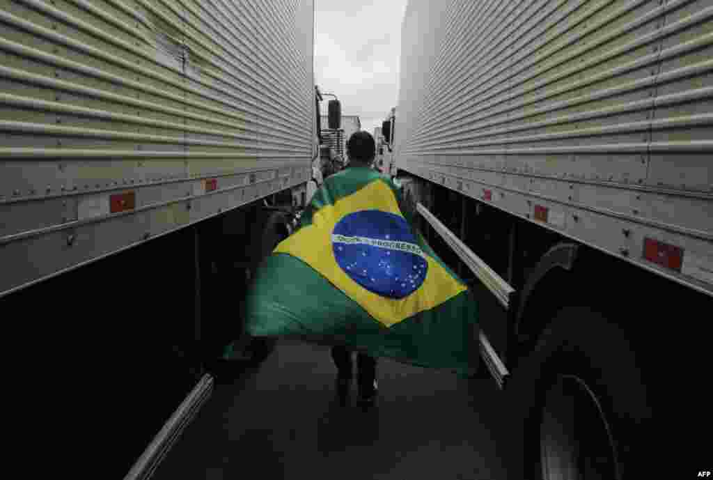 A supporter of President Jair Bolsonaro with a Brazilian flag walks between trucks during a blockade on Castelo Branco highway, on the outskirts of Sao Paulo, Brazil.
