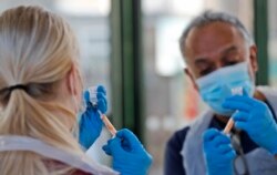 Dokter Anil Mehta melatih seorang perawat magang Ellie Bull, menyiapkan jarum suntik dengan dosis vaksin AstraZeneca di Welcome Center di Ilford, London timur, Jumat, 5 Februari 2021.