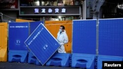 上海一名身穿防护服的工作人员站在封城使用的围栏旁。（2022年4月11日）