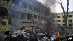 FILE - A car burns at the site of a maternity hospital damaged by shelling in Mariupol, Ukraine, March 9, 2022.