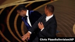 Will Smith, right, hits presenter Chris Rock on stage while presenting the award for best documentary feature at the Oscars on Sunday, March 27, 2022, at the Dolby Theatre in Los Angeles. (AP Photo/Chris Pizzello)

