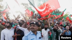 A police officer reacts as the supporters of Pakistani Prime Minister Imran Khan, chairman of the Pakistan Tehreek-e-Insaf (PTI) political party, wave flags as he lands from a helicopter to attend a public rally in Islamabad, Pakistan, March 27, 2022. 