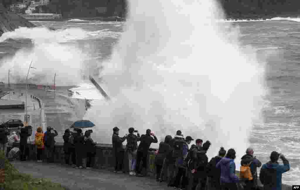 People watch waves crashing on a seaside promenade in the northern Spanish Basque city of San Sebastian.
