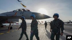 中国海军第二艘、也是第一艘完全由本国建造的002型山东号航母。照片显示山东号停泊在三亚军港，飞行员走在甲板上。-新华社照片