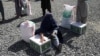 FILE - An Afghan woman waits to receive a food package distributed by a Saudi Arabia humanitarian aid group at a distribution center in Kabul, Afghanistan, April 25, 2022. 