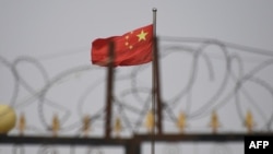 FILE - The Chinese flag flies behind razor wire at a housing compound in Yangisar, south of Kashgar, in China's western Xinjiang region, June 4, 2019.