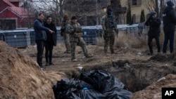 ARCHIVO - Personas junto a una fosa común en Bucha, en las afueras de Kiev, Ucrania, el 4 de abril de 2022. Periodistas de AP vieron decenas de cuerpos en Bucha, muchos de ellos disparados a quemarropa y algunos con las manos atadas a la espalda. . (Foto AP/Rodrigo Abd, Archivo)