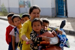 In this Sept. 20, 2018 file photo, a Uighur woman and children sit on a motor-tricycle after school at the Unity New Village in Hotan, in western China's Xinjiang region.