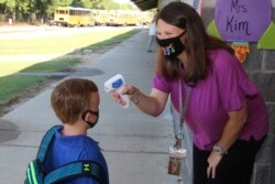 In a photo provided by Newton County Schools, teaching assistant Crystal May talks to kindergarten student Lewis Henry Thompson, 5, as she takes his temperature at Newton County Elementary School in Decatur, Mississippi, Monday, Aug. 3, 2020.