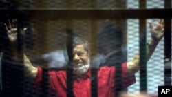 FILE - Former Egyptian President Mohammed Morsi, wearing a red jumpsuit that designates he has been sentenced to death, raises his hands inside a defendants cage in a makeshift courtroom at the national police academy, in an eastern suburb of Cairo.