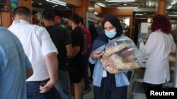 People queue as a woman carries several loafs of bread at a bakery in Beirut, Lebanon, June 29, 2022.